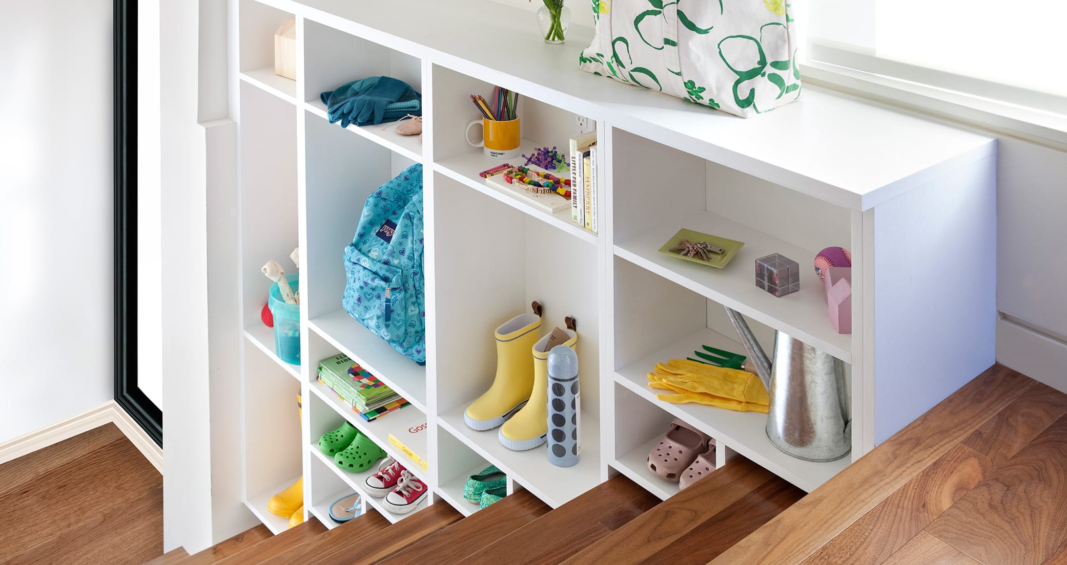 White tiered storage cubbies for kids shoes up the stairs California Closets