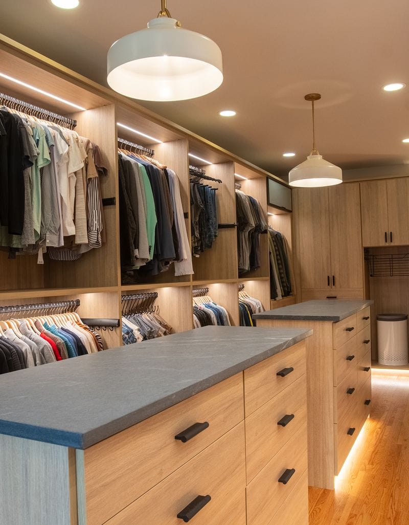 Long walkway walk in closet design with center islands led lighting and custom cabinets in natural wood finish by California Closets
